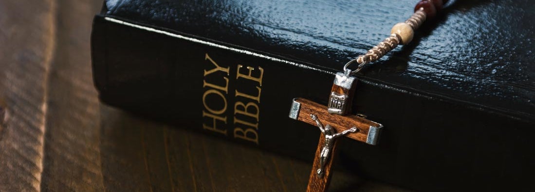 Holy Bible with crucifix on wooden table of religious supply store