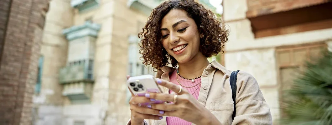 Woman with curly brown hair looking at smart phone. Find Cell Phone Insurance.