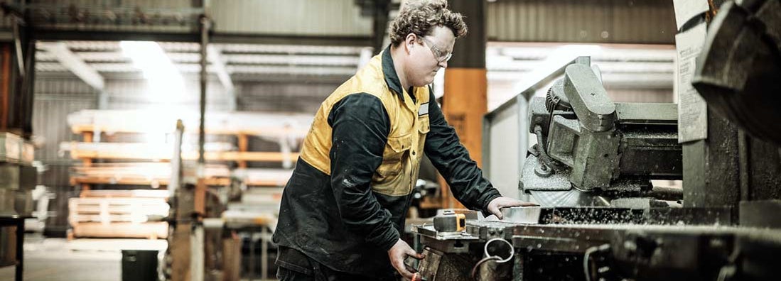 Blue collar worker in factory cutting metal parts. Workers' compensation for employees.