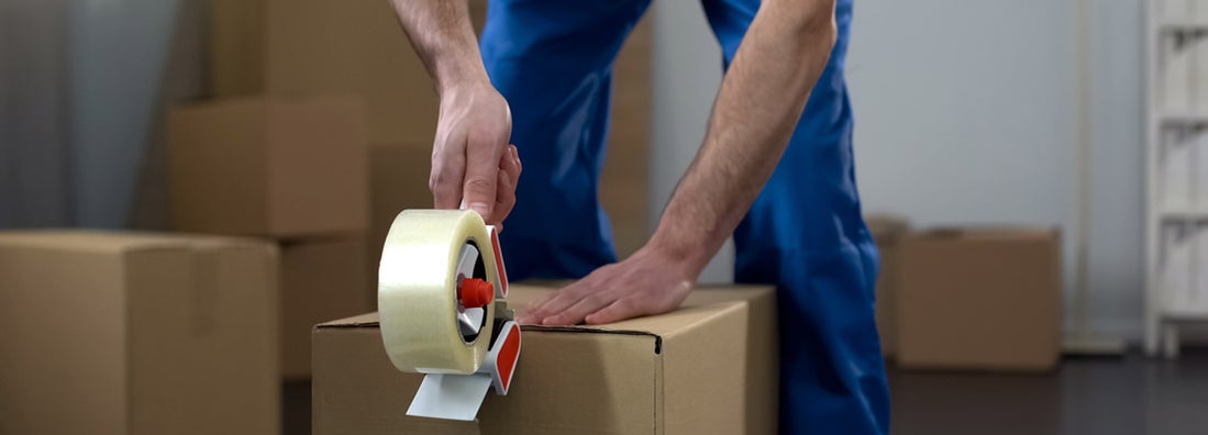 Moving company worker packing cardboard boxes, quality delivery services. Find moving insurance.