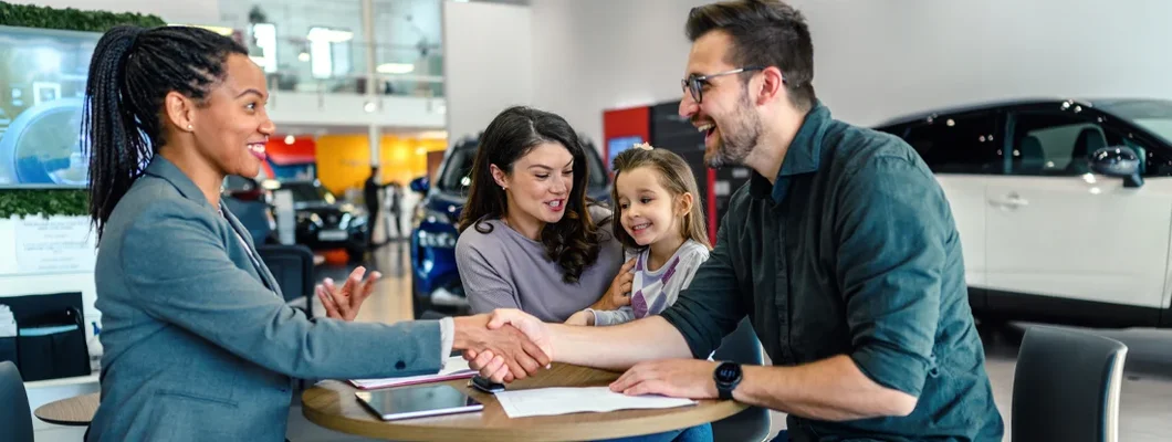 Happy family came to an agreement with a car salesperson at a meeting in a showroom. How to Get a Car Loan the Easy Way.
