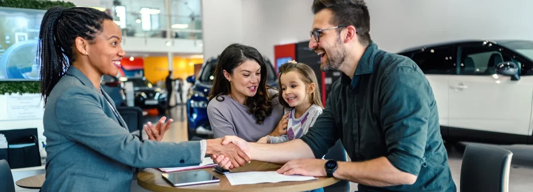 Happy family came to an agreement with a car salesperson at a meeting in a showroom. How to Get a Car Loan the Easy Way.