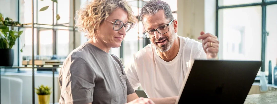 Couple with Coffee Using Laptop in Bright Dining Area. Find Pre-Existing Conditions Insurance.