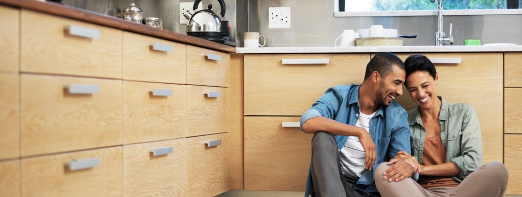 Smiling young couple sitting together on kitchen floor on condo. Find Wyoming condo insurance.