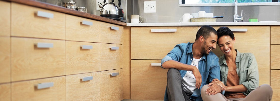 Smiling young couple sitting together on kitchen floor on condo. Find Wyoming condo insurance.