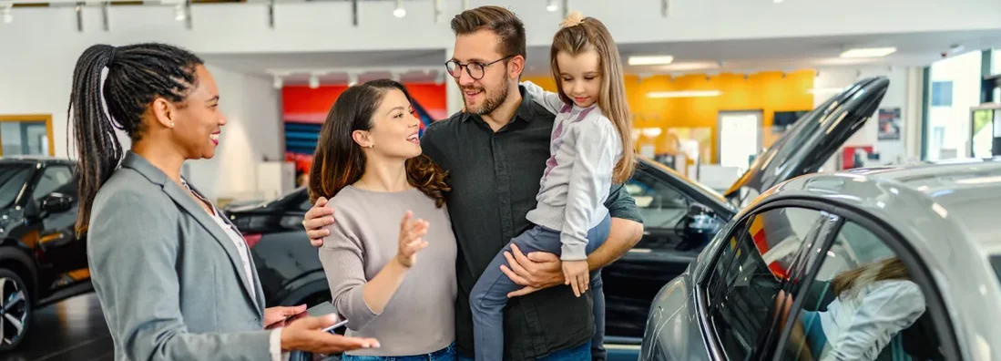 Saleswoman at car dealership center helping family lease a new vehicle. Guide to Leasing a Car.