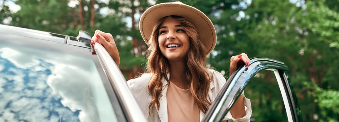 Woman in a hat stands near the car on the background of the forest. Find Woodstock, Georgia car insurance.