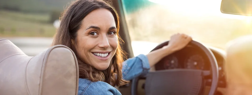 Woman holding steering wheel ready to drive and looking back. Car Insurance in Coppell, Texas.