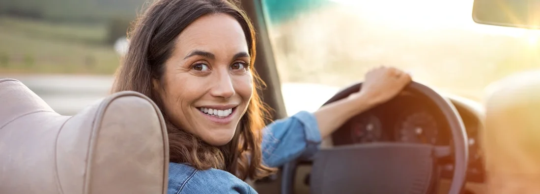 Woman holding steering wheel ready to drive and looking back. Car Insurance in Coppell, Texas.