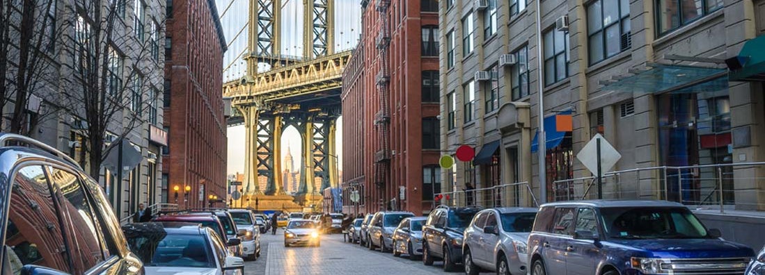 Manhattan Bridge between renovated warehouses at sunset. Find Brooklyn New York car insurance.