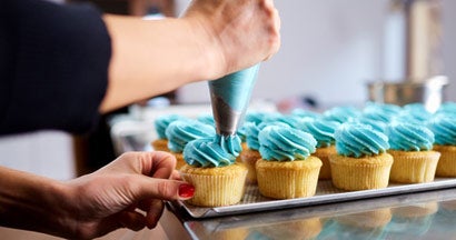 Woman in bakery icing cupcakes. Find business liability insurance.