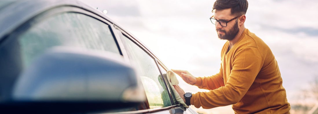 Young man cleaning the windows on his car outside. How to Find the Best Car Insurance in Madison, SD. 