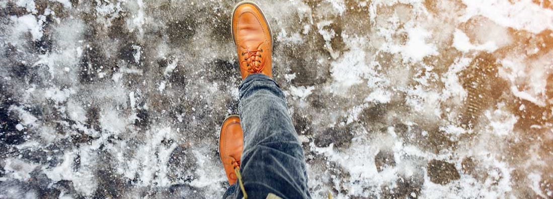 Feet of a man walking along the icy pavement. Who’s Responsible for an Icy Sidewalk Slip and Fall?