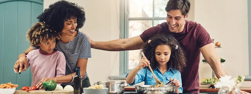 Family of four cooking together in their kitchen at home. Term vs. Permanent Life Insurance. 