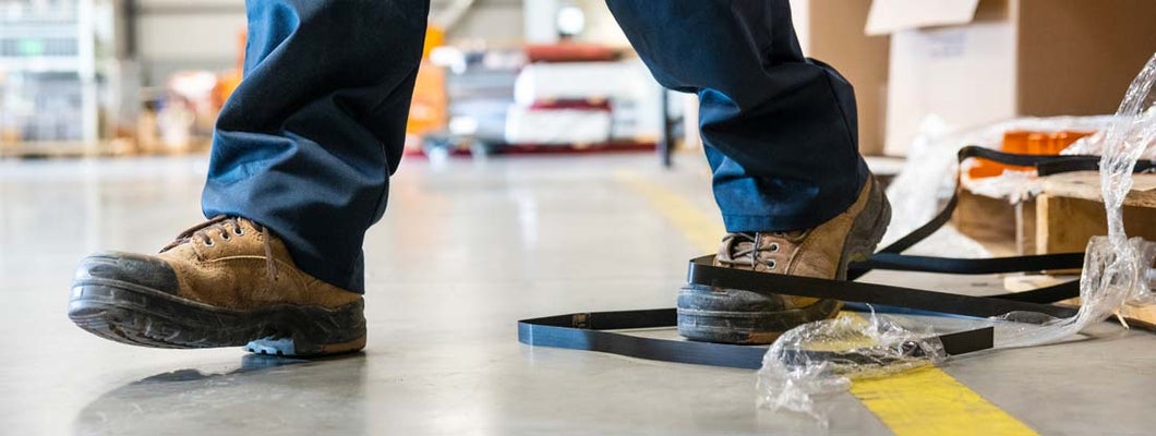 A worker in danger of tripping over a piece of metal strapping in a factory.