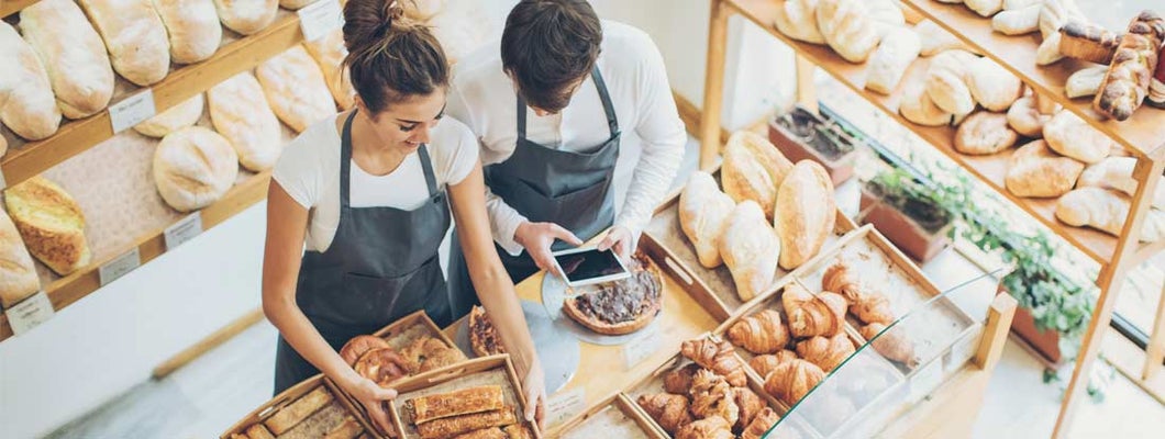 Top view of bakers inside the bakery, holding a digital tablet and arranging the pastries