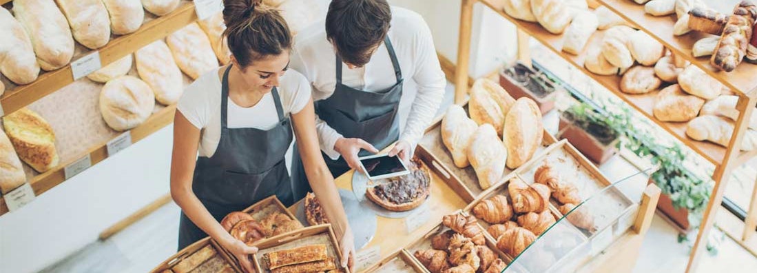 Top view of bakers inside the bakery, holding a digital tablet and arranging the pastries