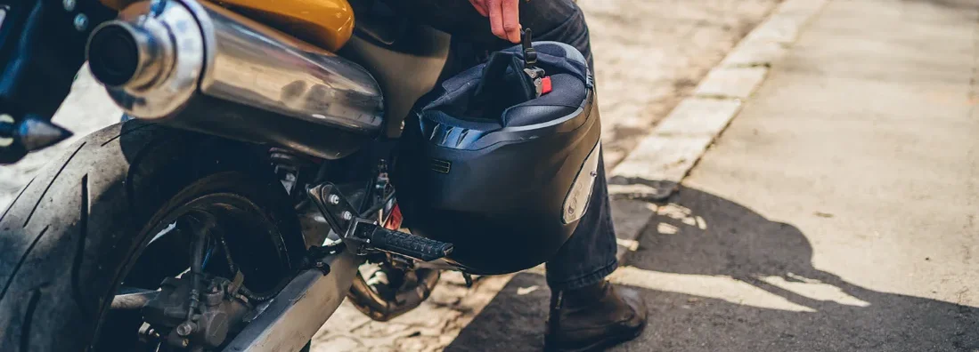 Biker man sitting on motorcycle, holding crash helmet. Find Mississippi Motorcycle Insurance.