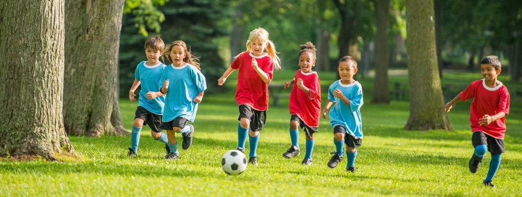 Little kids playing soccer outside at summer sports camp