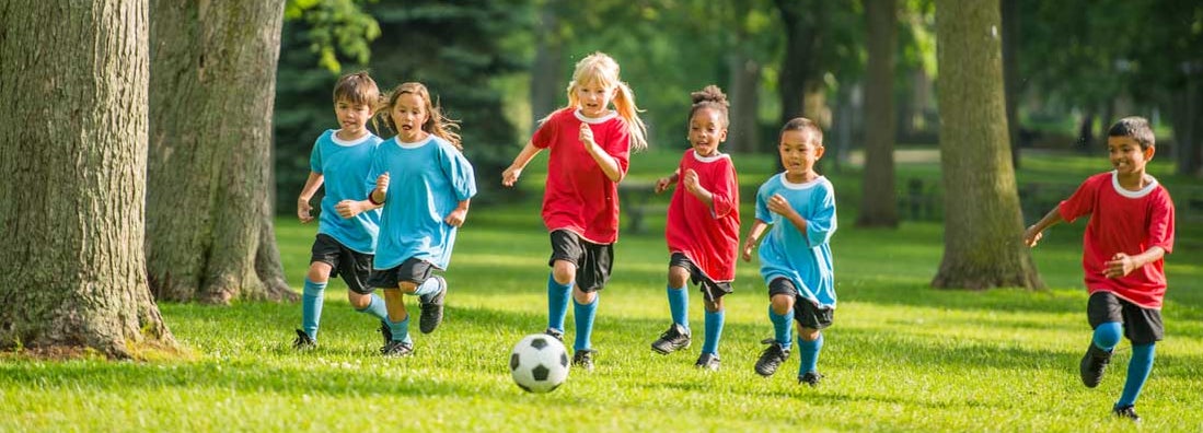 Little kids playing soccer outside at summer sports camp