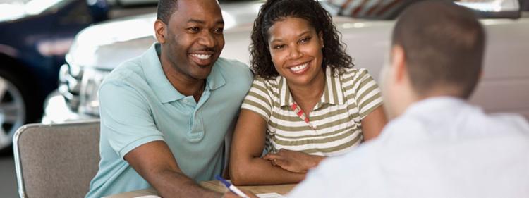 Happy couple working on paperwork at a car dealership.