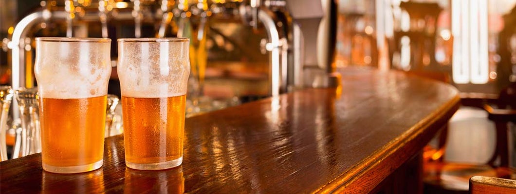Two ice cold glasses of beer on wooden counter of bar. Find the best bar insurance with an independent insurance agent.