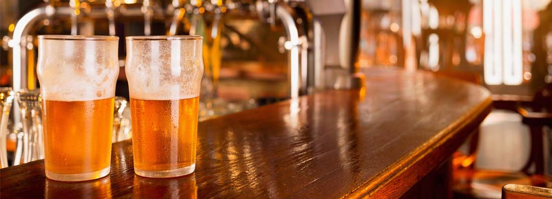 Two ice cold glasses of beer on wooden counter of bar. Find the best bar insurance with an independent insurance agent.