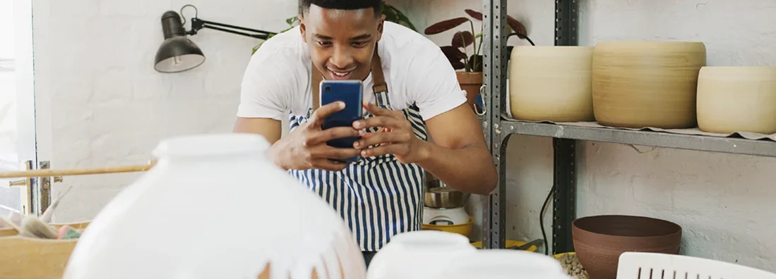 Man taking pictures of his finished products with a smartphone in a pottery studio. Business Insurance in Broadview Heights, Ohio.