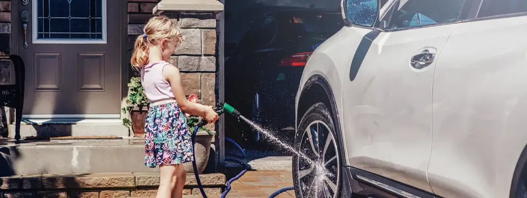 Girl washing car on driveway in front house on summer day. How to find the Best Umbrella Insurance in South Carolina.