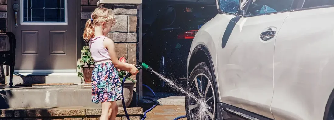 Girl washing car on driveway in front house on summer day. How to find the Best Umbrella Insurance in South Carolina.