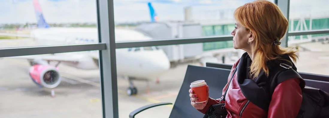 Times When Travel Insurance Is a Must-Have. Woman sitting at the gate waiting room with traveling documents and coffee. 