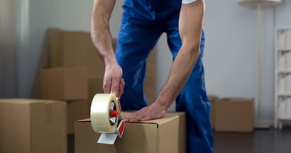 Moving company worker packing cardboard boxes, quality delivery services. Find moving insurance.