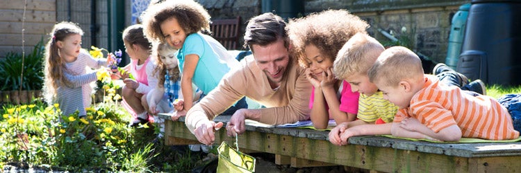 Children enjoying an outdoors lesson on nature with their daycare teacher.