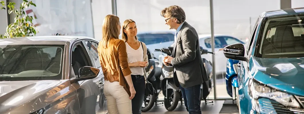 Female customers having a conversation with a salesman standing next to new cars at a car dealership. What is the best time to buy a car?