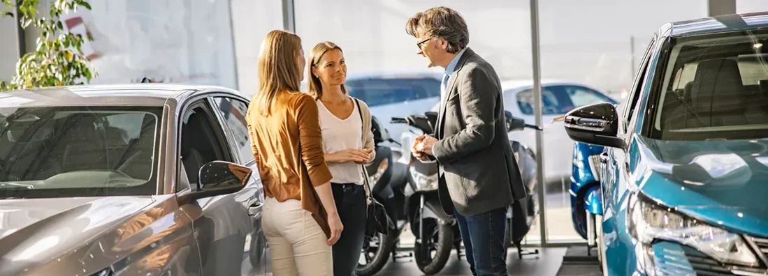 Female customers having a conversation with a salesman standing next to new cars at a car dealership. What is the best time to buy a car?