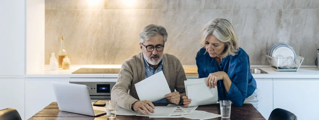 Mature couple with papers and laptop on kitchen table at home. Is Long-Term Care Insurance Tax-Deductible?