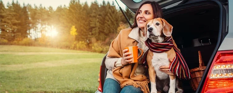 Woman and dog sit together in car trunk in autumn. Best cars under $10,000.