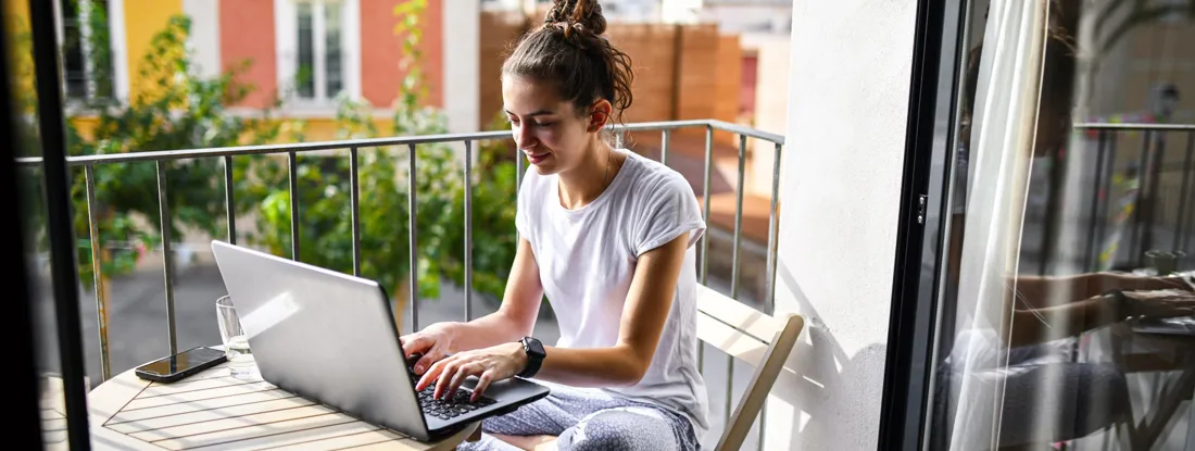Female working on a laptop from apartment balcony. Renters Insurance Claims.