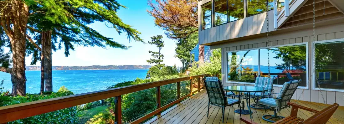 Wooden walkout deck with outdoor table set and swinging bench at lake house. Seven Essential Considerations Before Buying That Gorgeous Lake House.