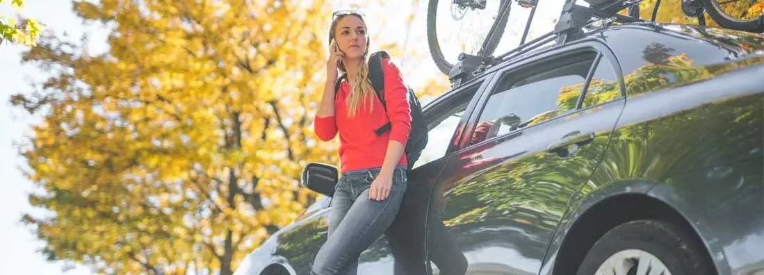 Woman standing next to car with bicycles on the car roof rack and using her phone. Get car insurance quotes.