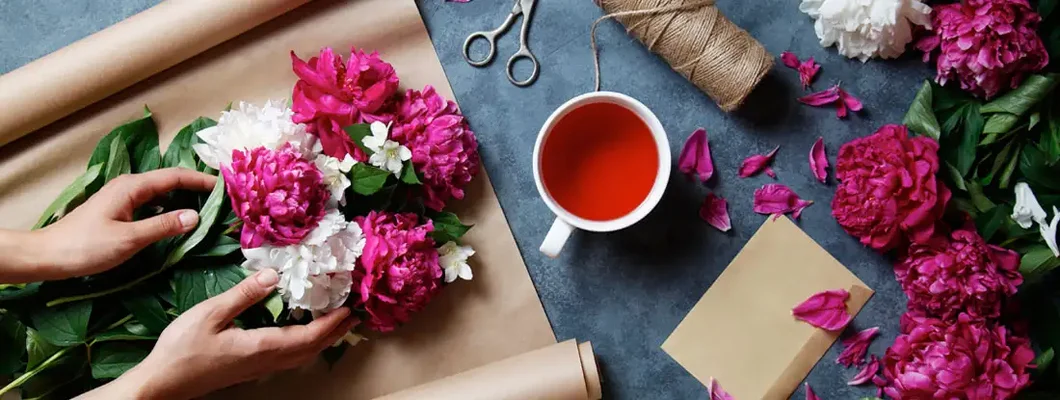 Florist making summer bouquet of peonies on a working gray desk. Find Florists Insurance.