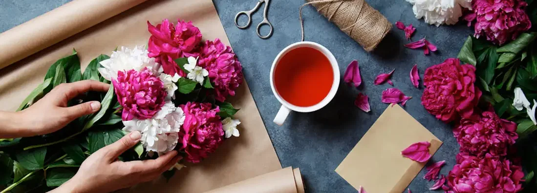 Florist making summer bouquet of peonies on a working gray desk. Find Florists Insurance.