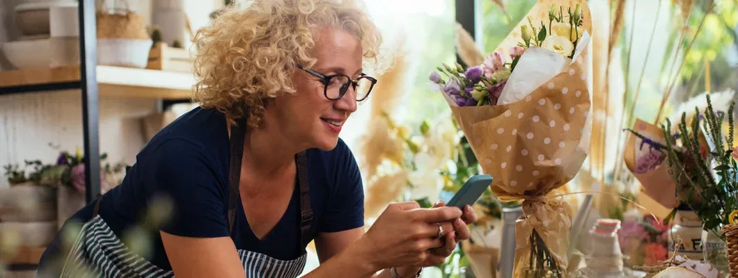 Blond woman using a cellphone while working in her flower shop. Find Warwick Rhode Island business insurance.