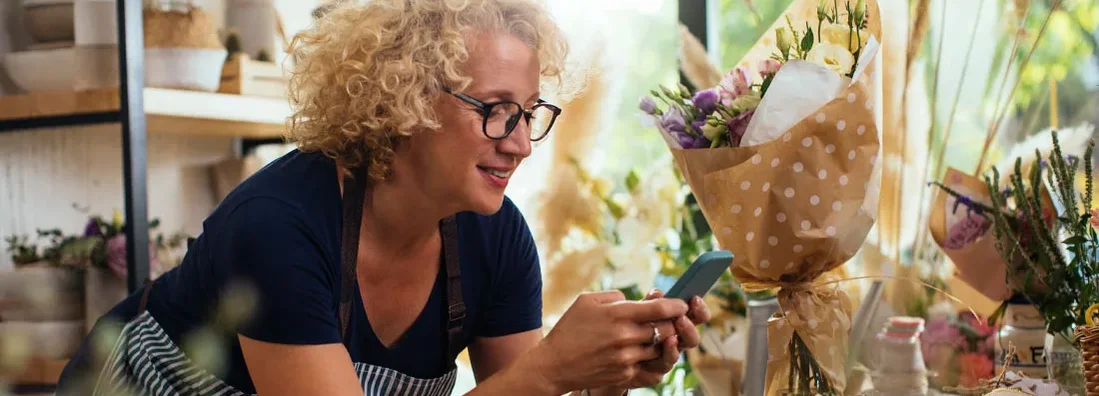 Blond woman using a cellphone while working in her flower shop. Find Warwick Rhode Island business insurance.