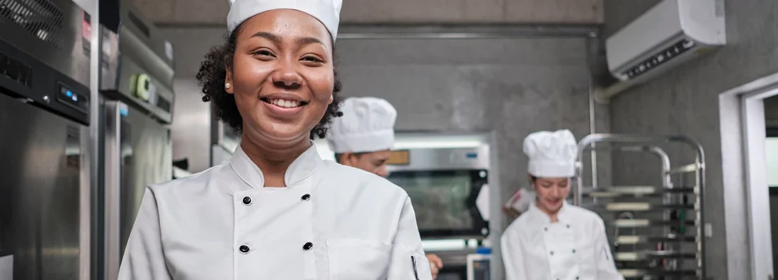 African American female chef looks at camera with a cheerful smile in a kitchen. How to Find the Best Business Insurance in Lenexa, Kansas.
