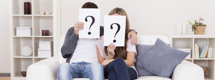 A couple holds up question marks in front of their faces.