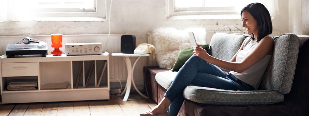 Woman sitting on sofa using digital tablet. Find Idaho renters insurance.