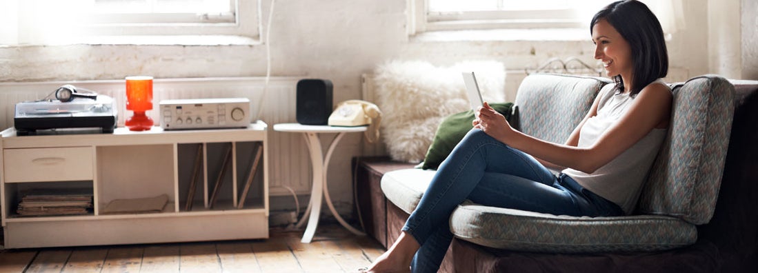 Woman sitting on sofa using digital tablet. Find Idaho renters insurance.