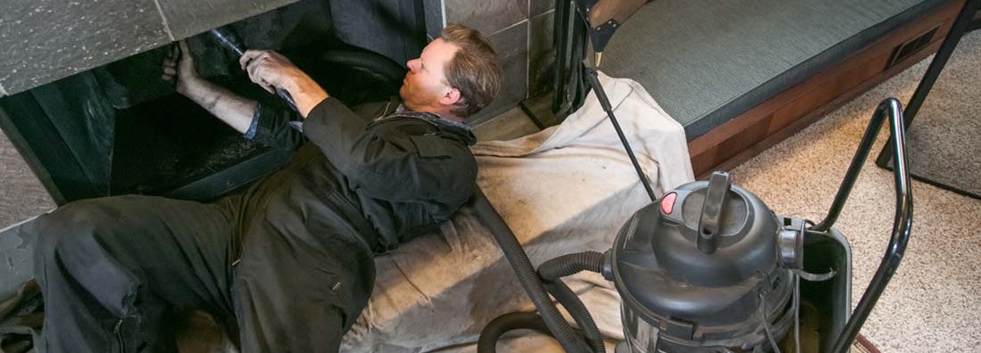 Chimney sweeper cleaning fireplace inside of home. Find Chimney Sweeper Insurance.