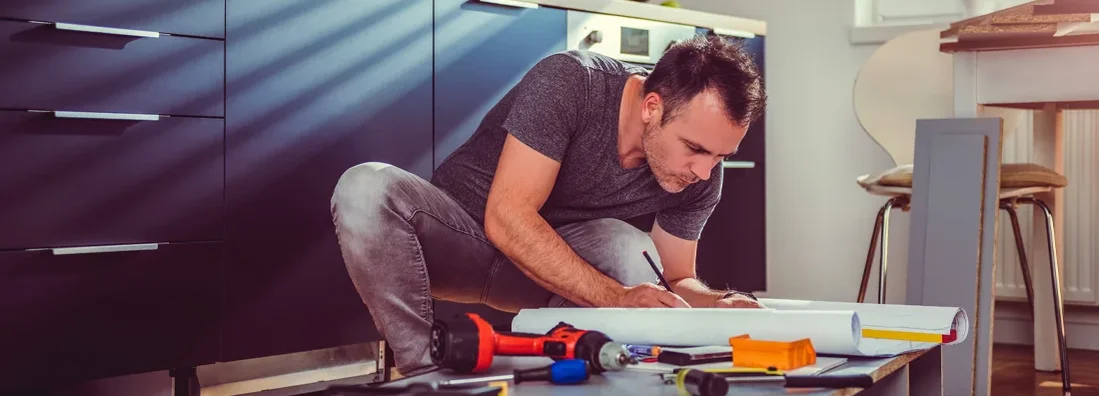 Man checking blueprints while building kitchen cabinets. 6 Major Home Renovations that Impact Your Homeowner’s Insurance Needs.